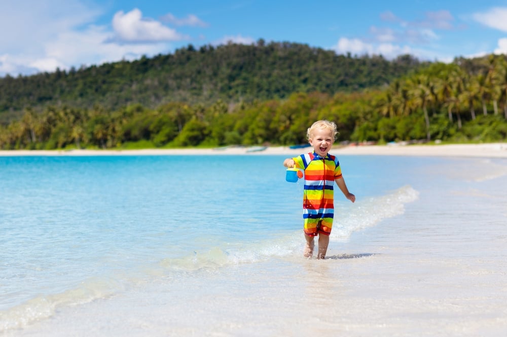 Child running on beach in rainbow swimsuit