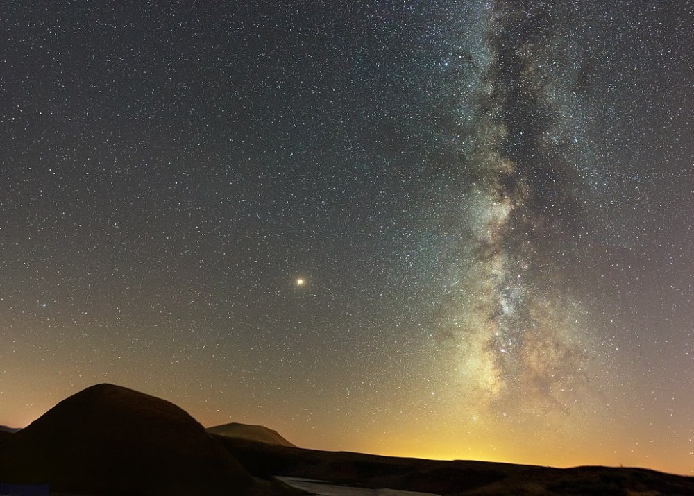 Gorgeous stars over the silhouette of a mountain with a faint glimmer of a lake