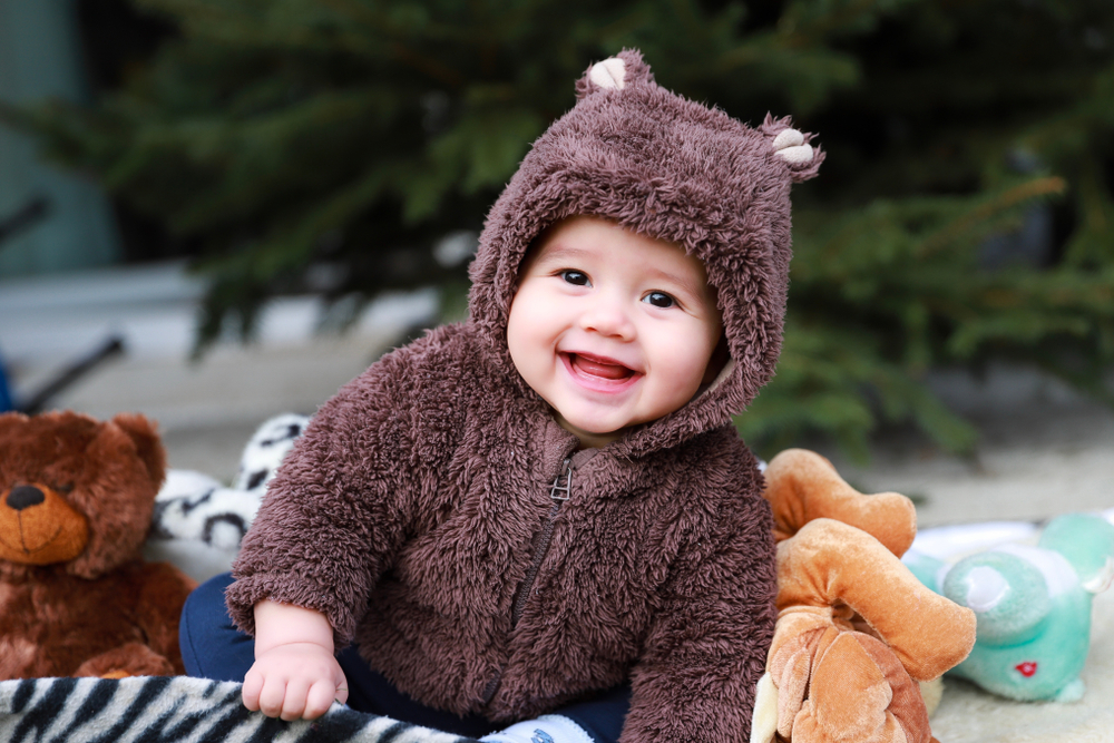 Baby with bear hat on sits in front of a tree