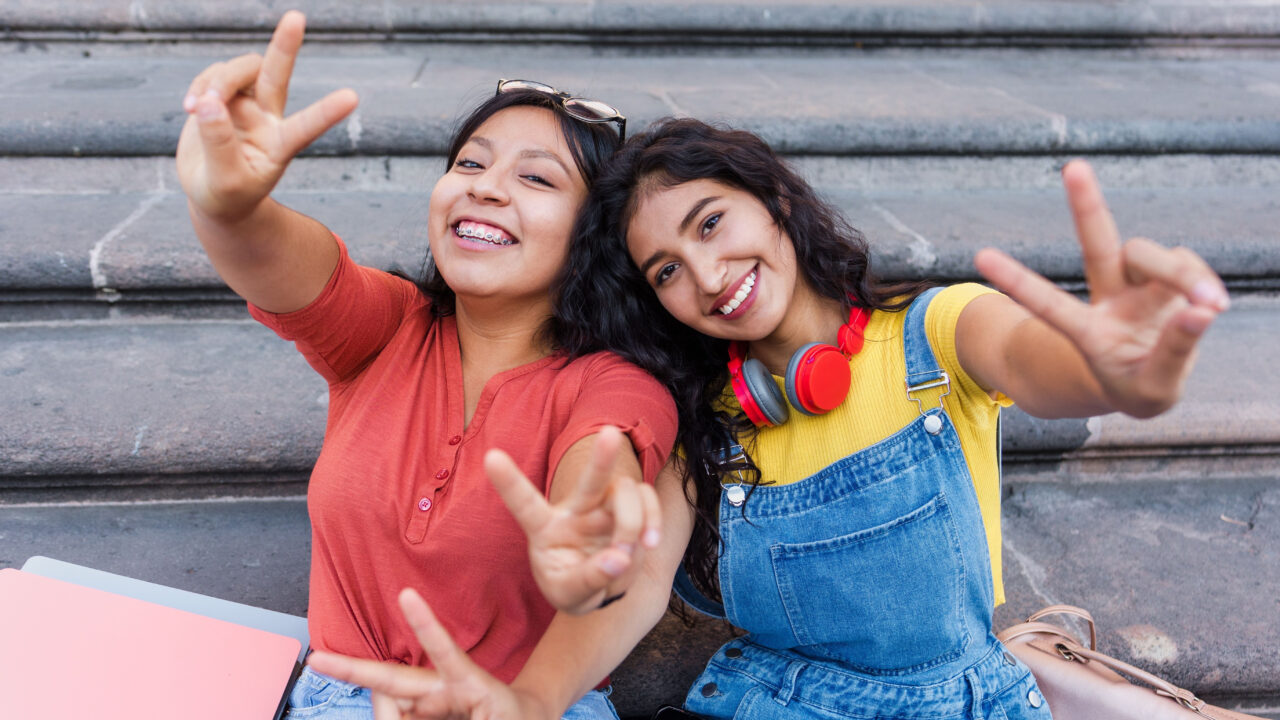 Two happy friends showing peace signs.