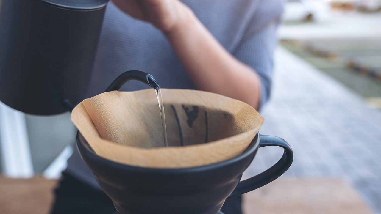 Person pouring hot water into drip coffee setup.