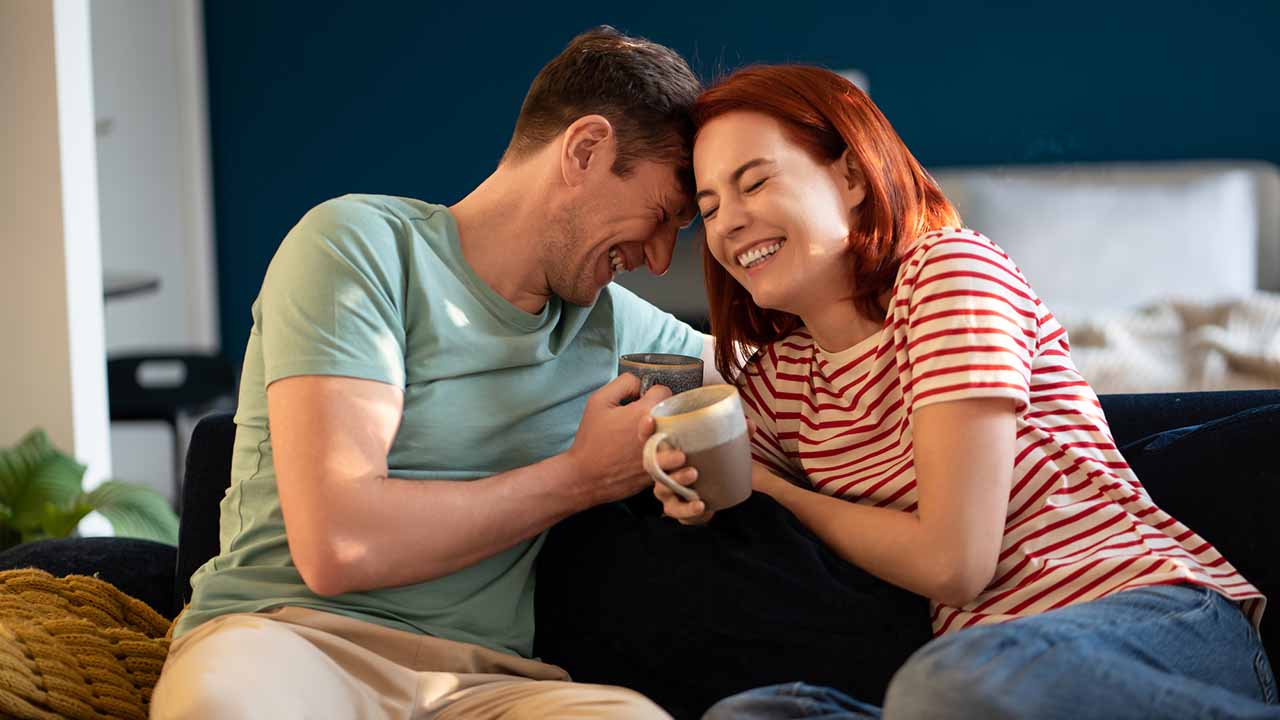 Couple laughing together over a cup of coffee on the couch.