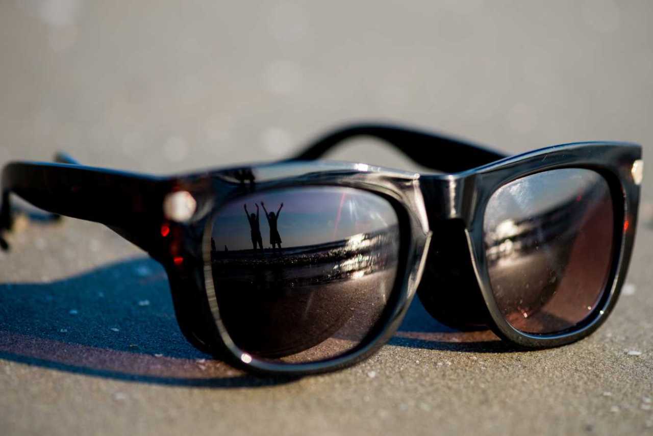 Happy people on beach reflected in sunglasses.